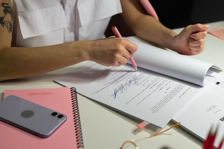 Close-up of a person writing on documents at a well-organized office desk.