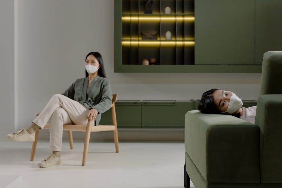 Two Asian women wearing face masks practice social distancing inside a modern home environment.