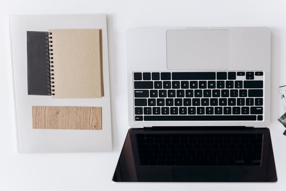 Top view of a minimalist workspace with a laptop and notebooks on a white desk.