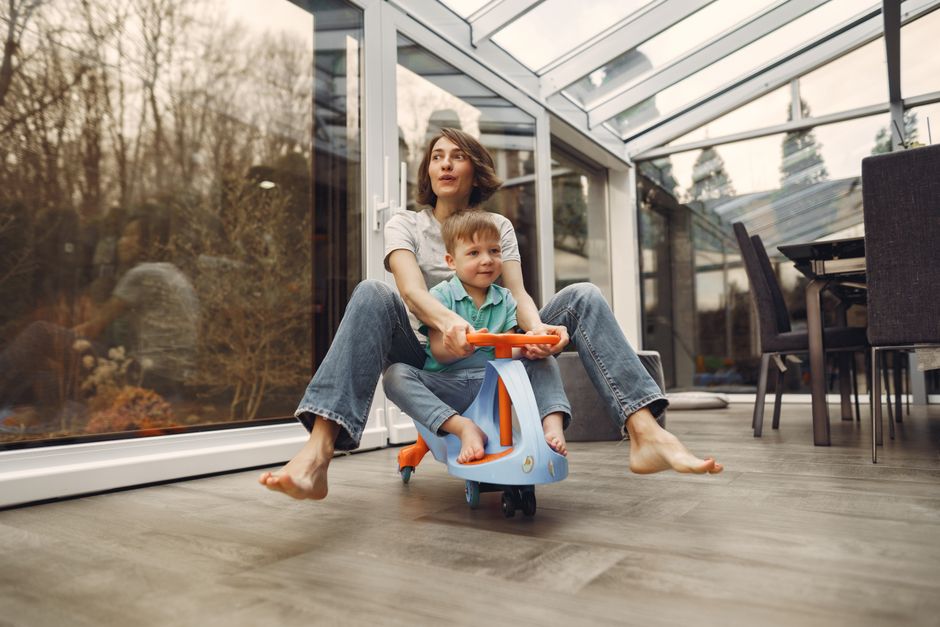A joyful mother and son bonding while playing on a toy car indoors, exuding fun and happiness.