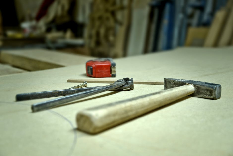 Close-up of hammer, screw, pincers, and tape measure on a workbench in a workshop.