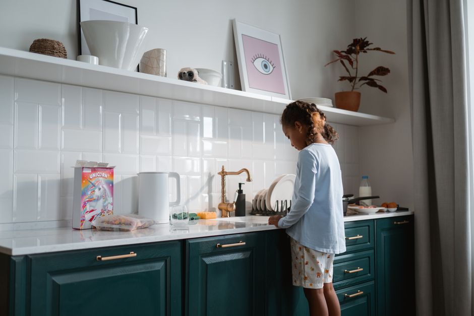 Young girl washing dishes at kitchen sink. Bright and cozy morning ambiance.