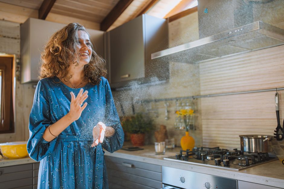 A joyful woman baking in a bright kitchen, flour floating in the air.