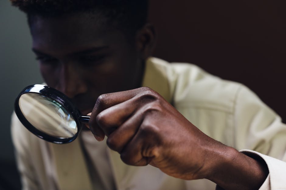 A man closely inspects an object using a magnifying glass.